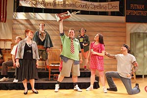Scene where performers are lifting the trophy from the 25th Annual Putnam County Spelling Bee.